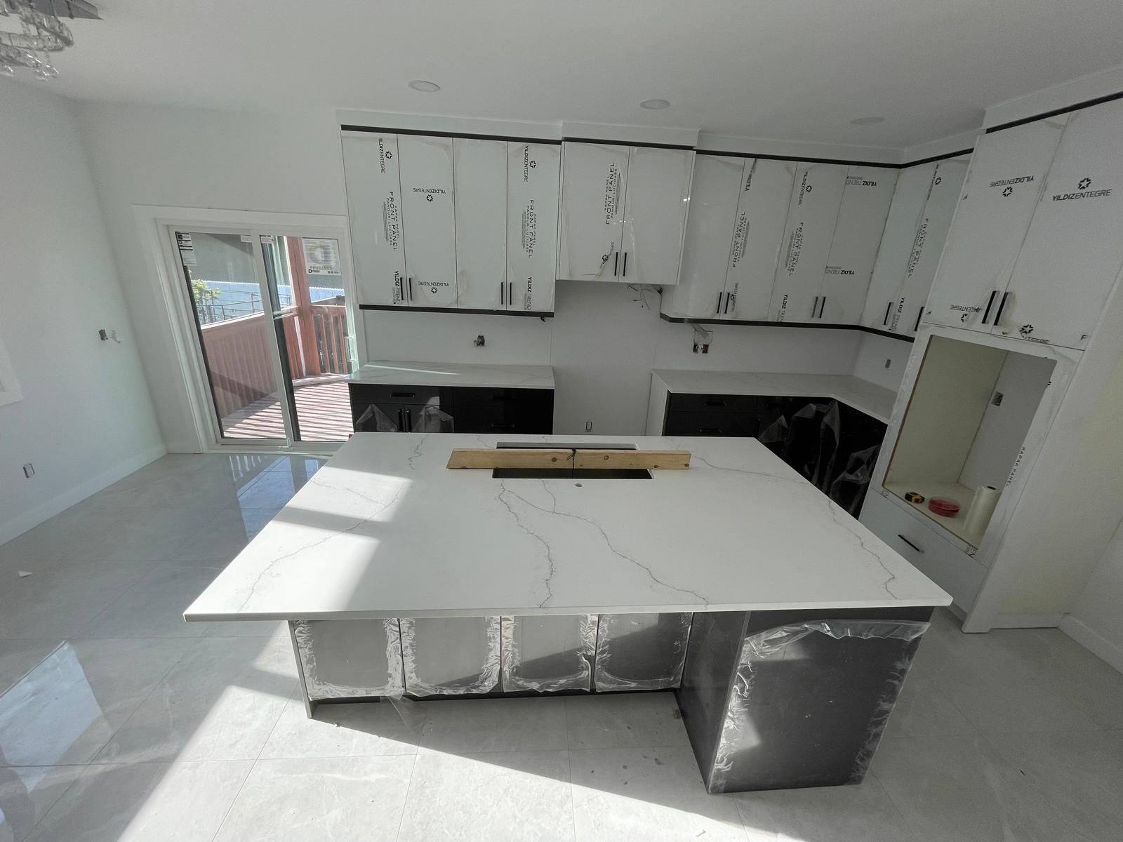 White cabinet kitchen with black base island and marble-look quartz under construction