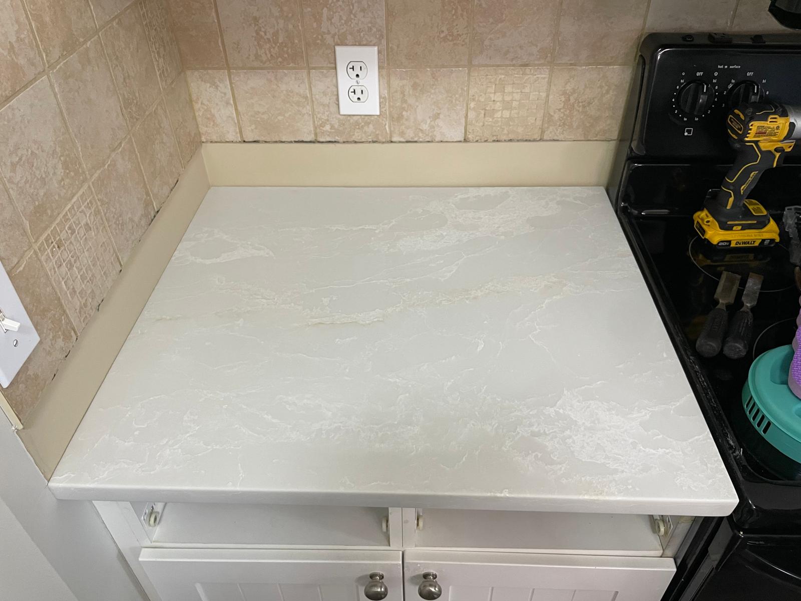 White quartz countertop installation in compact kitchen beside stove